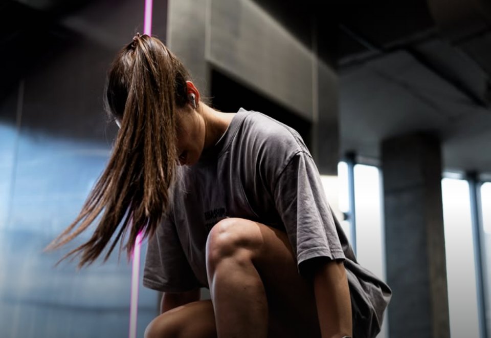 Site da Arena Academia, com uma aluna agachada ao lado de halteres sob luz de neon rosa