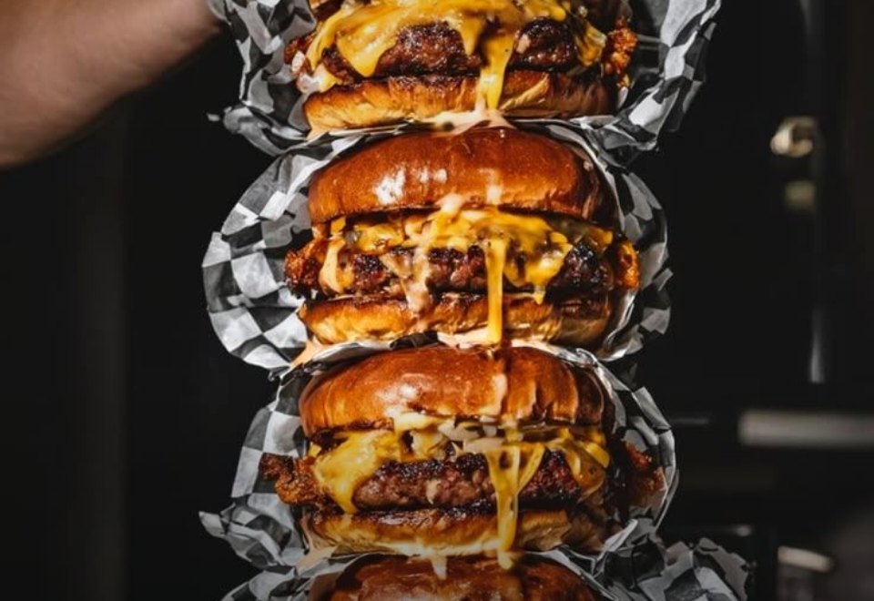 Site da Buzz Burg Burgers, com uma torre de smash burgers com cheddar derretido embrulhados em papel xadrez